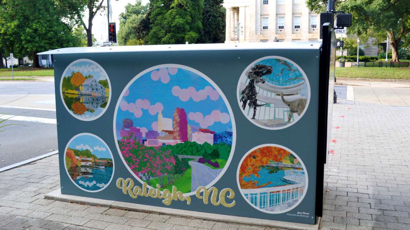 Artwork on a news rack kiosk that features scenes from Raleigh including the skyline, museums, and parks