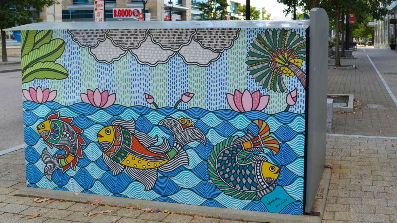 Artwork on a news rack kiosk done in a traditional style of folk art from India that features a colorful underwater scene with fish and plants.