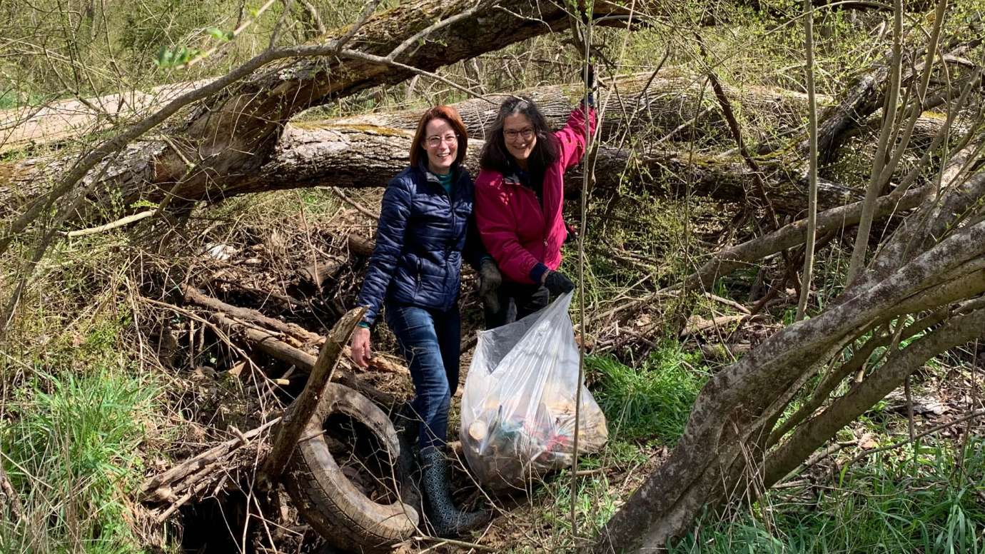 Two women standing near the streambank of Walnut Creek picking up trash.