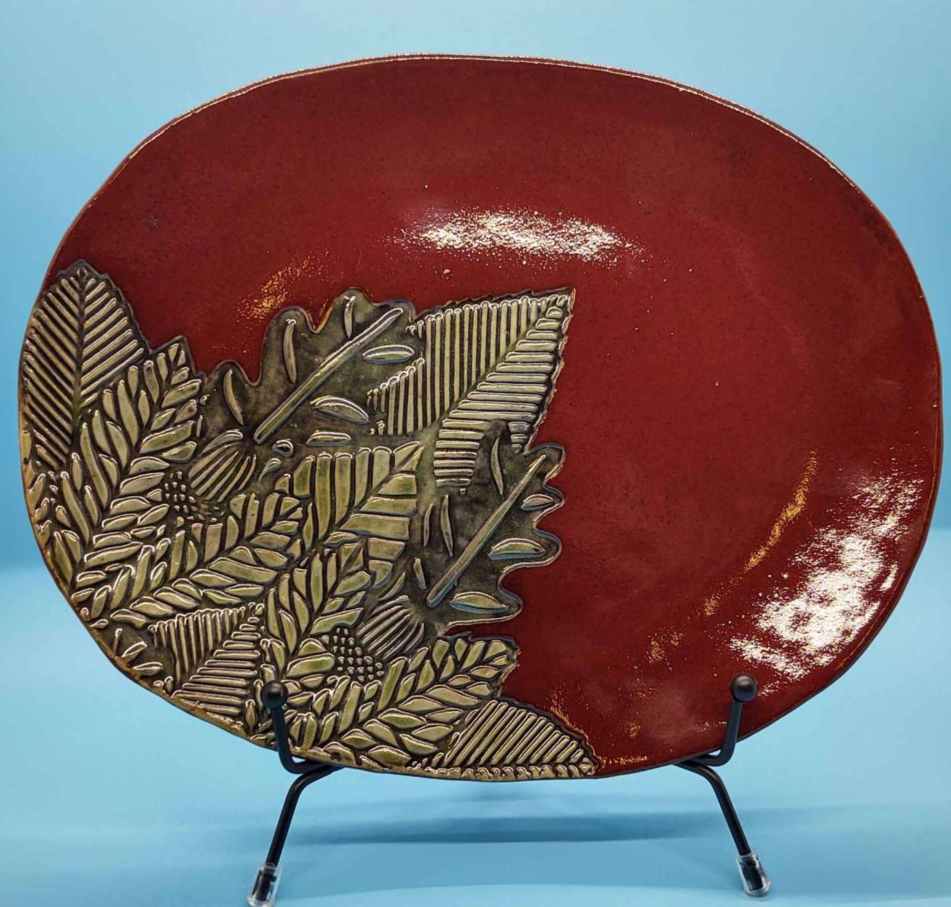 A photo of a red ceramic plate with green and beige leaves on it