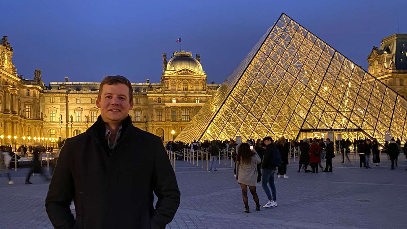Man smiling in front of glass pyramid of Louvre museum
