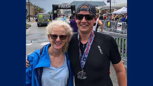 Man wearing medal smiling with arm around woman in front of finish line