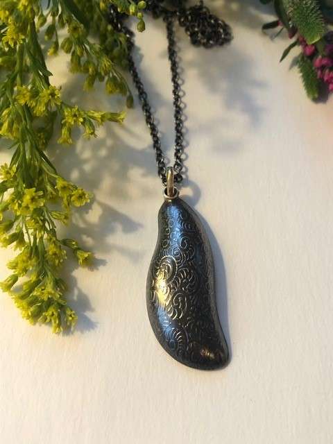 A necklace with an oblong, slightly curved black textured pendant