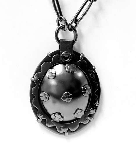 A dark metal pendant with small metal flowers on it