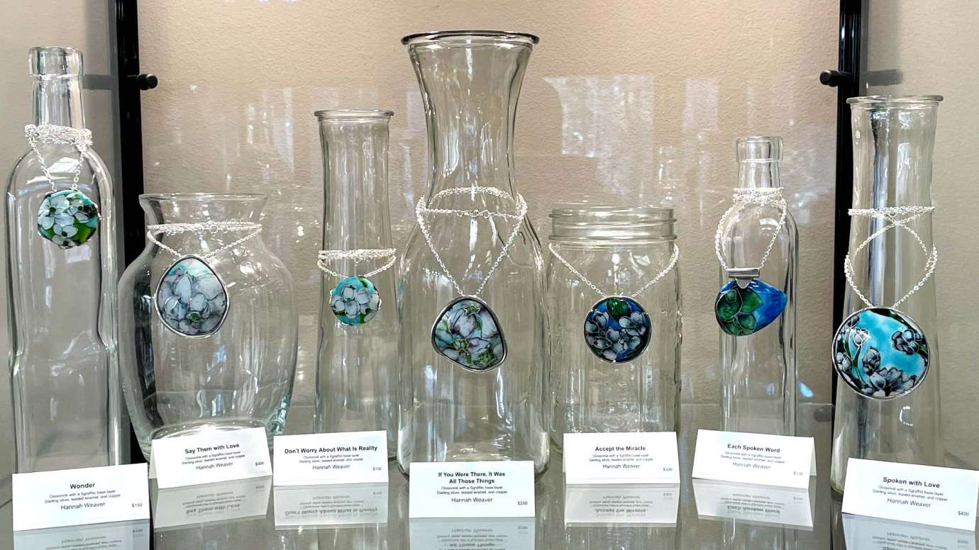 Necklaces with vibration blue and green swirled pendants hang off glass bottles in a glass display case