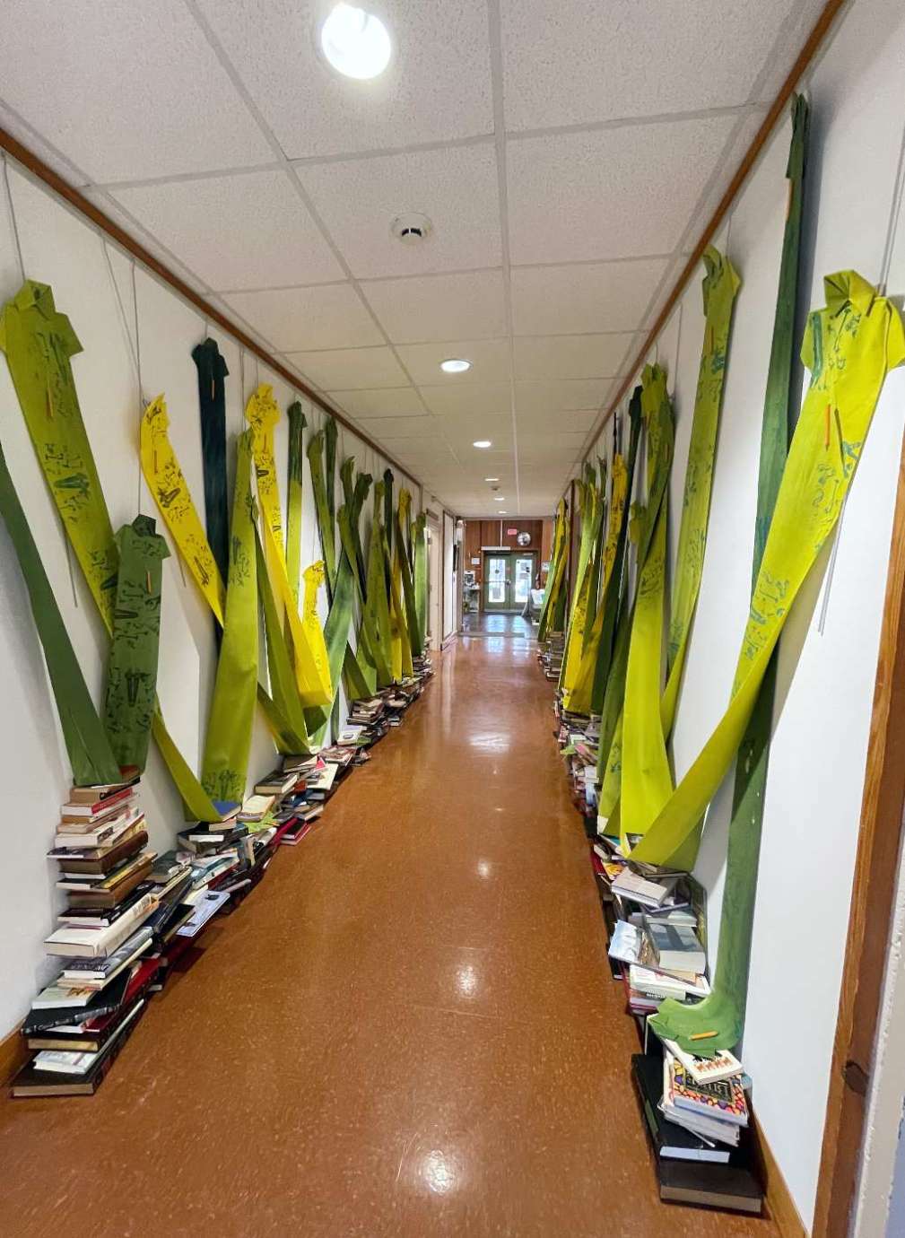 Jan-Ru Wan's installation which includes long hanging green shirts draping down the wall and supporting stacked books on the ground