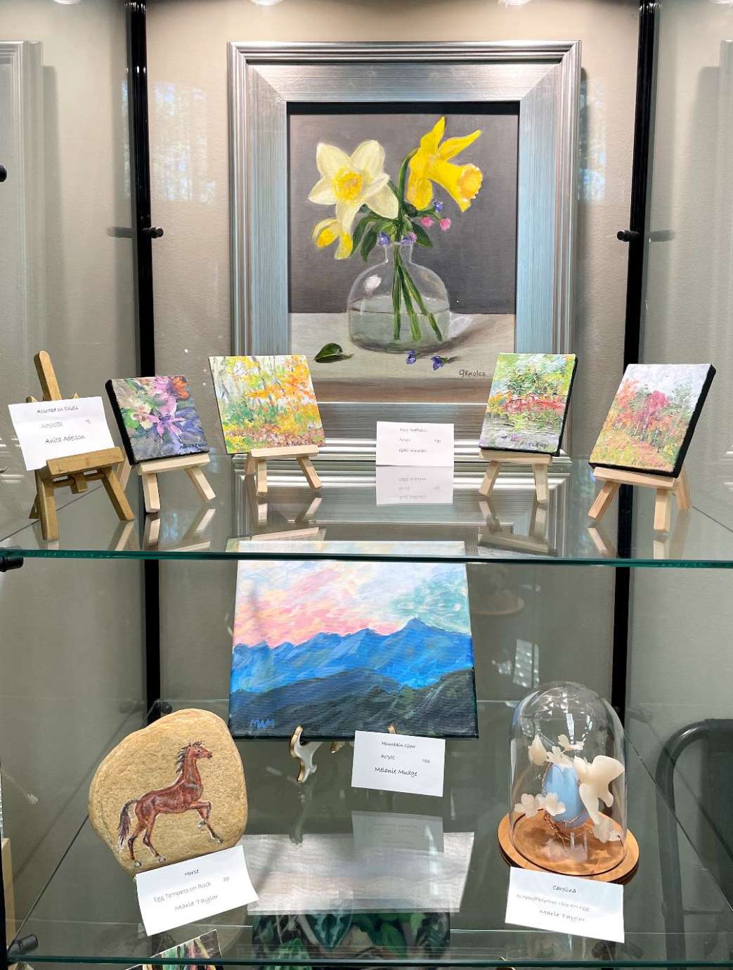 Artwork on display in a multi-shelf glass display case at Sertoma Arts Center