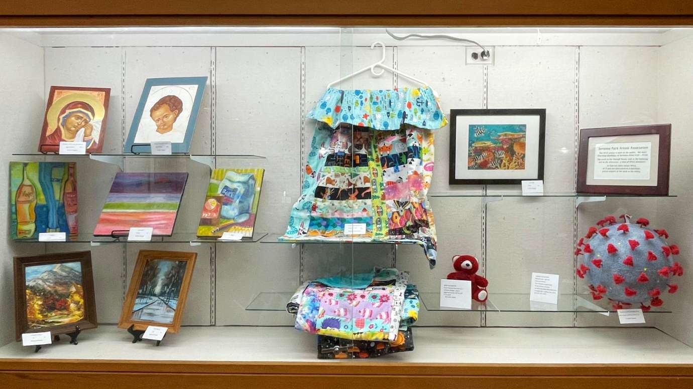 Artwork on display in a large multi-shelf glass display case at Sertoma Arts Center