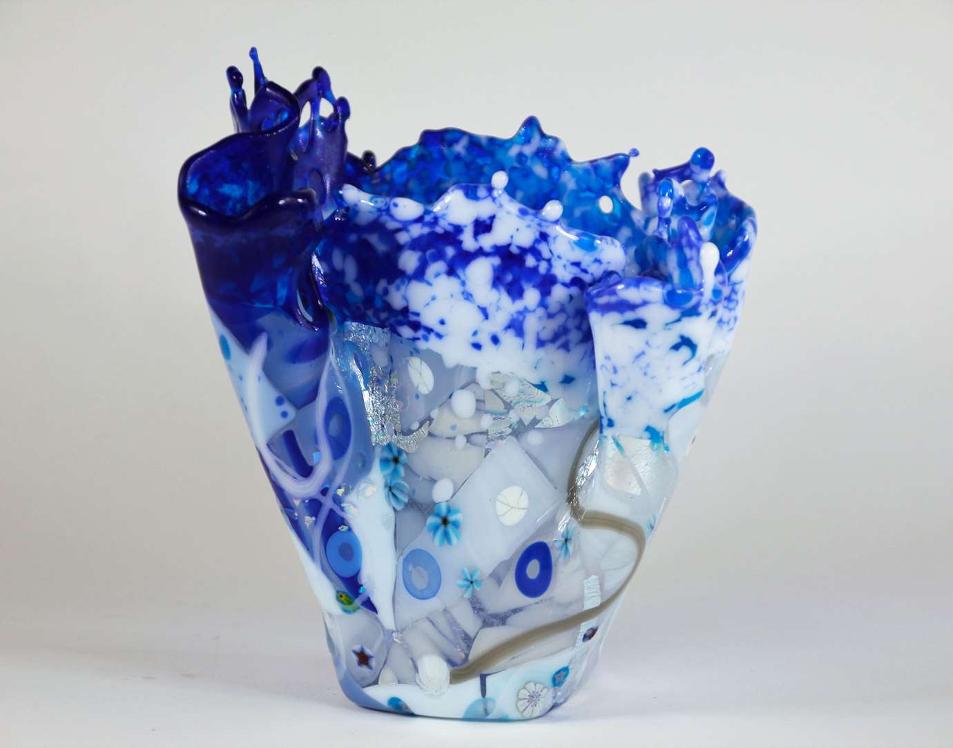 A blue, clear, white and silver folded glass vase with a wide mouth