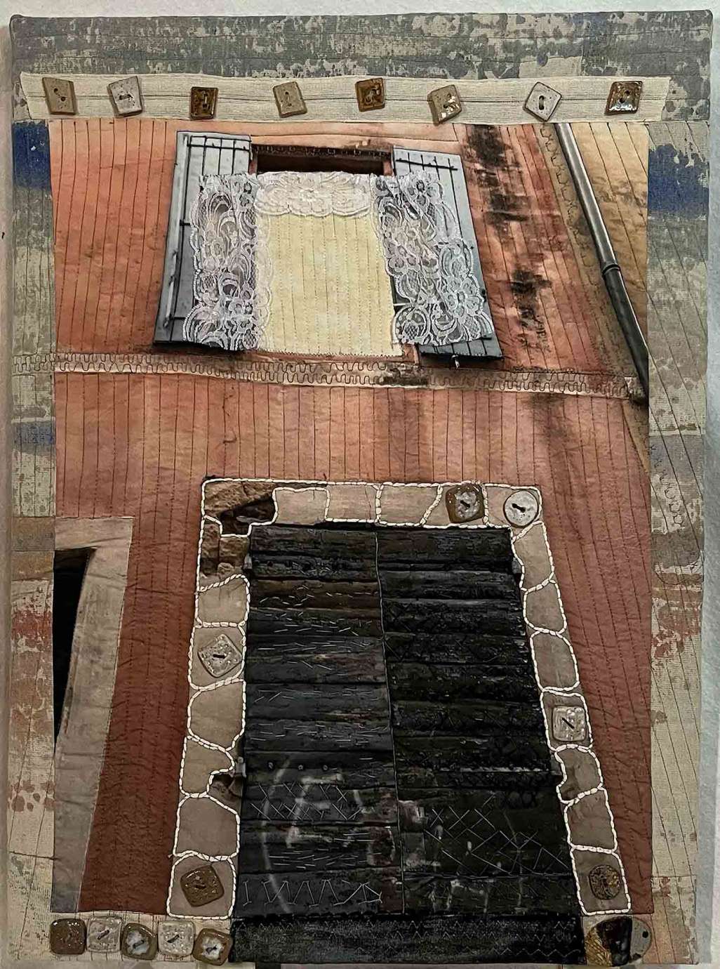 A quilt depicting the front of a red building with a lit open window above a dark door