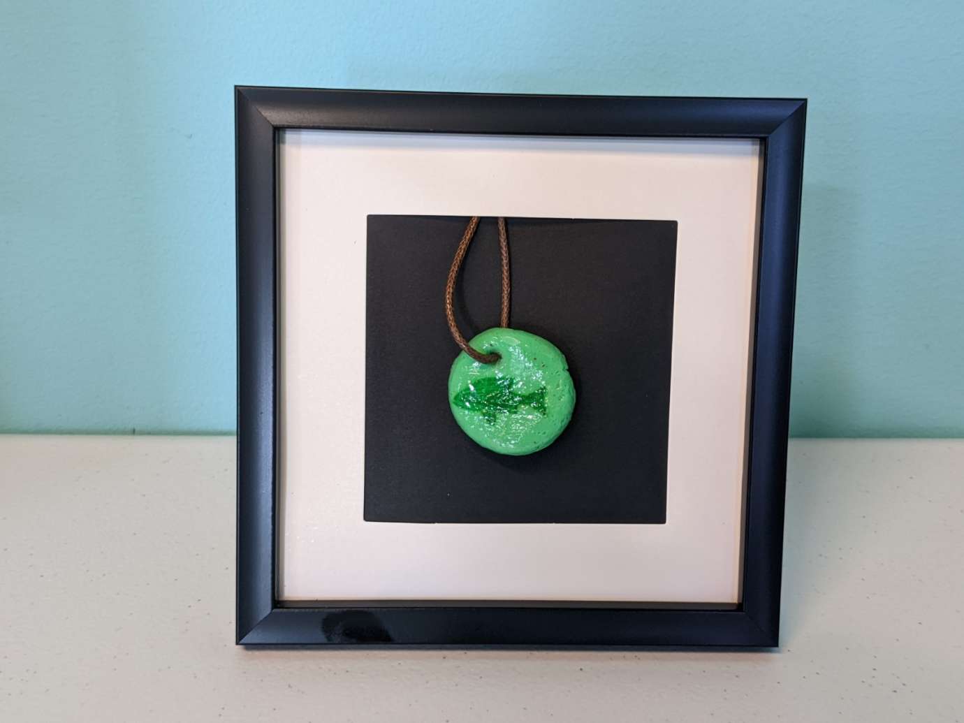 A framed green pendant necklace made by a member of the Abound Health Day Program