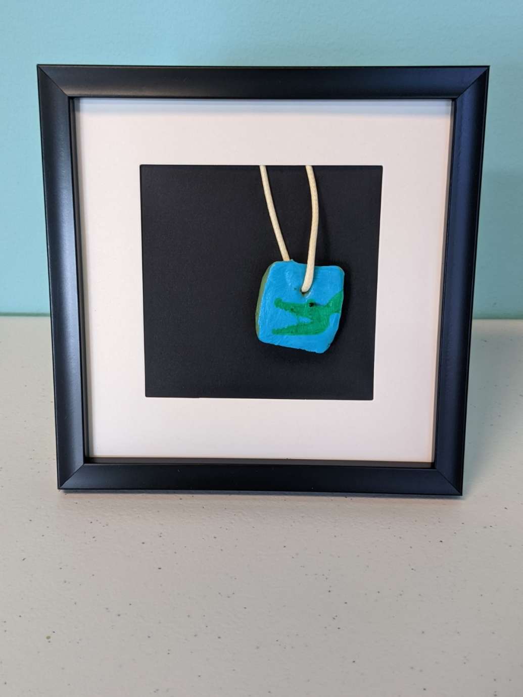 A framed blue pendant necklace made by a member of the Abound Health Day Program