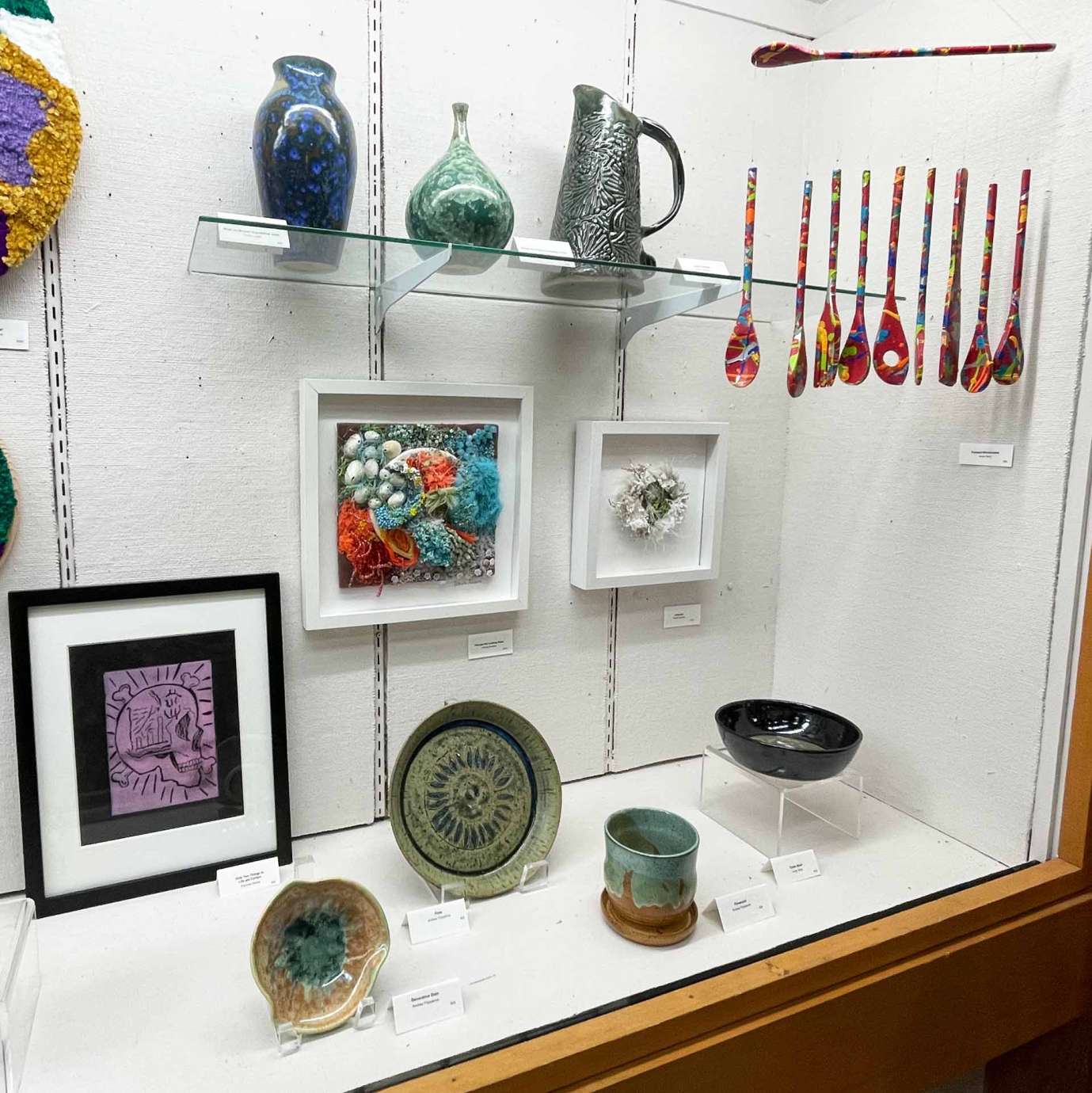 Various artist made items displayed on glass shelves within a case