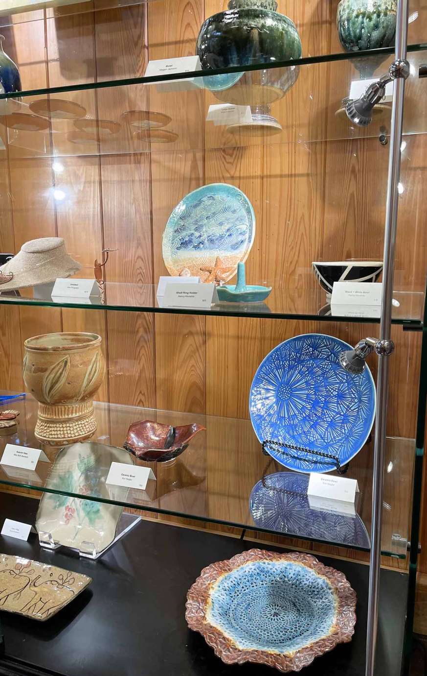 Various artist made items displayed on glass shelves within a case