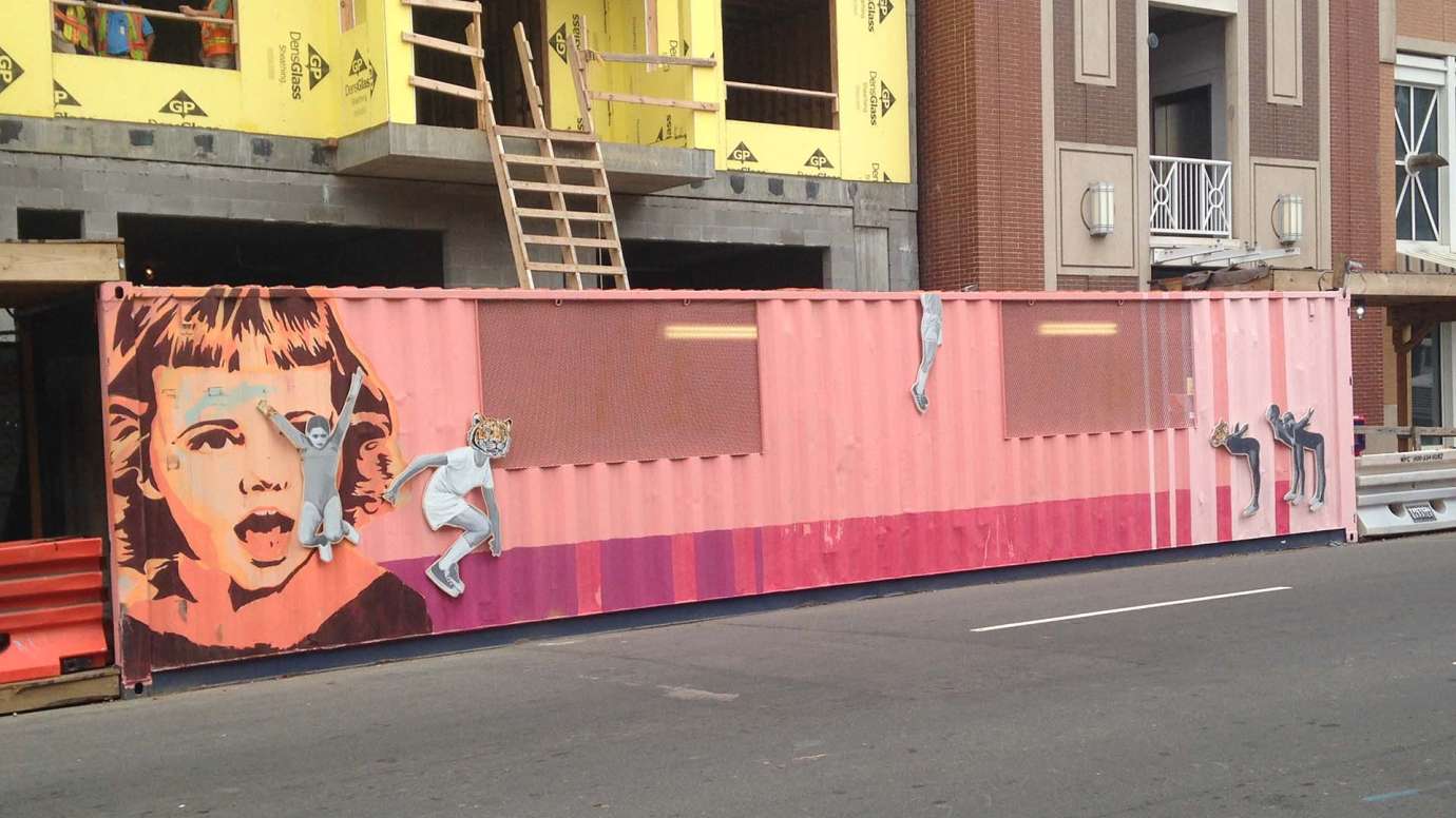 a temporary covered walk way painted pink with images of people attached