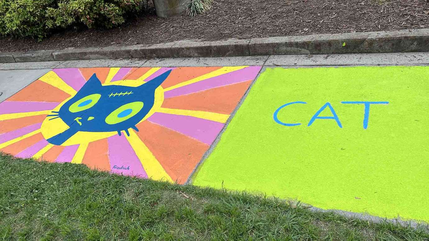 A sidewalk mural of a cartoon cat with the word cat next to it in neon green