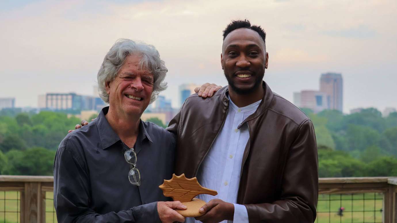 Two members of Wakeup Wake County pose with award with Raleigh skyline in background