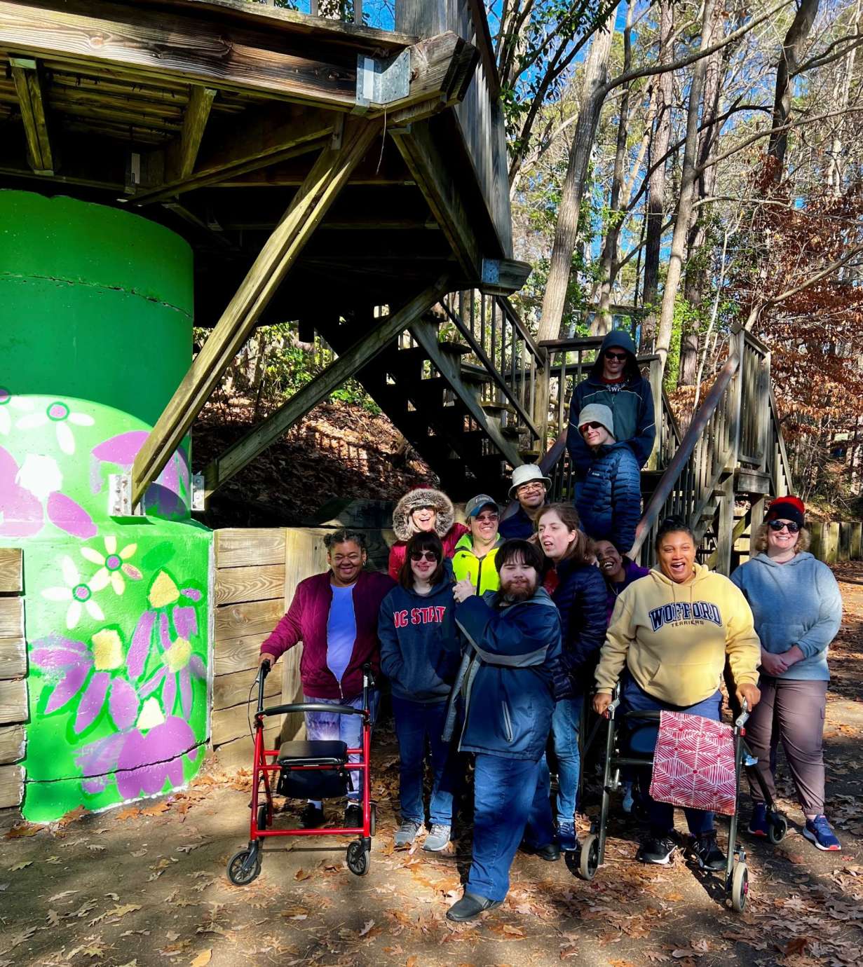 A group of smiling people outside on a trail excited to have just finished painting a mural