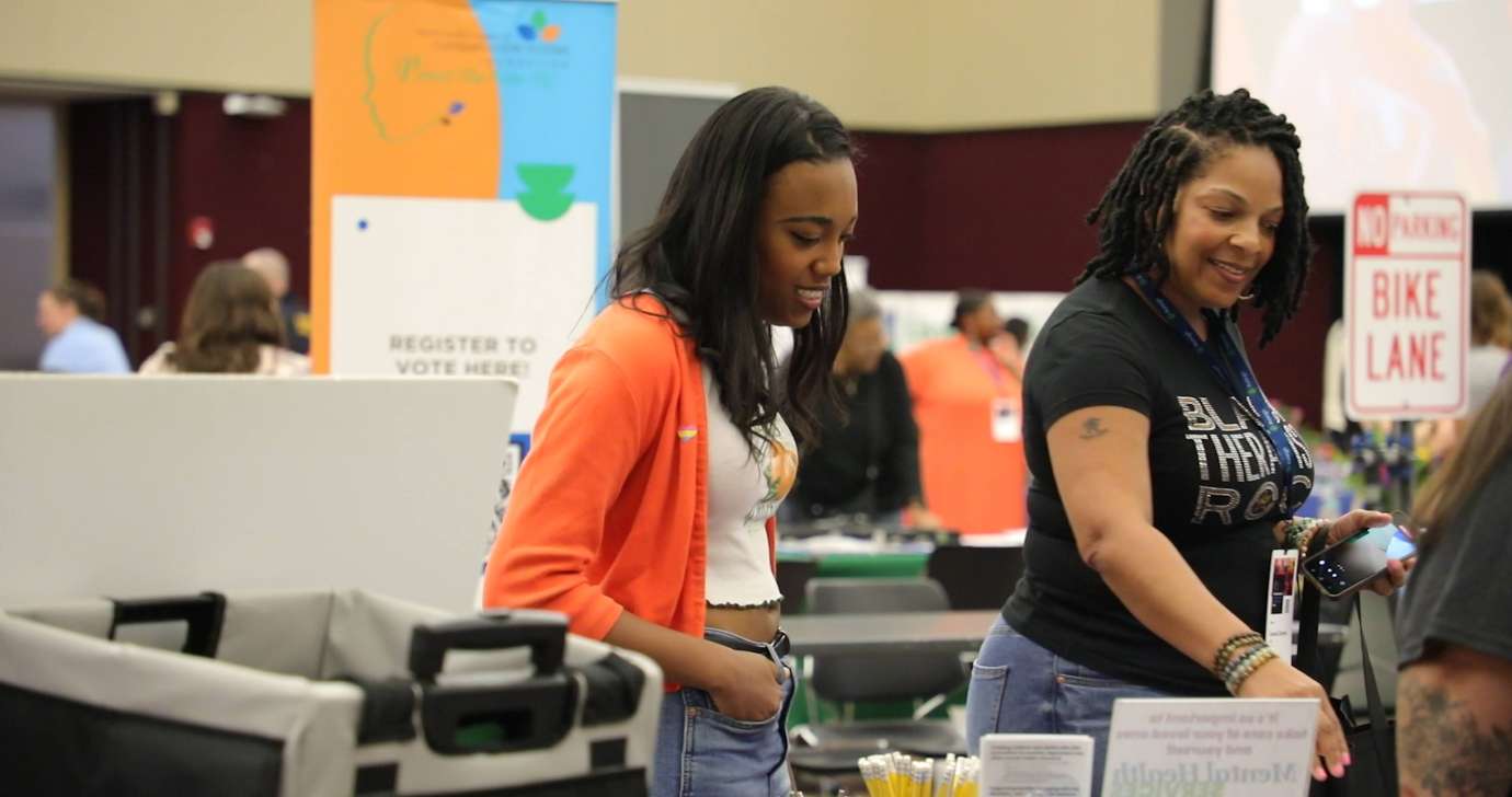 Two young ladies chat with staff at a table in the expo hall