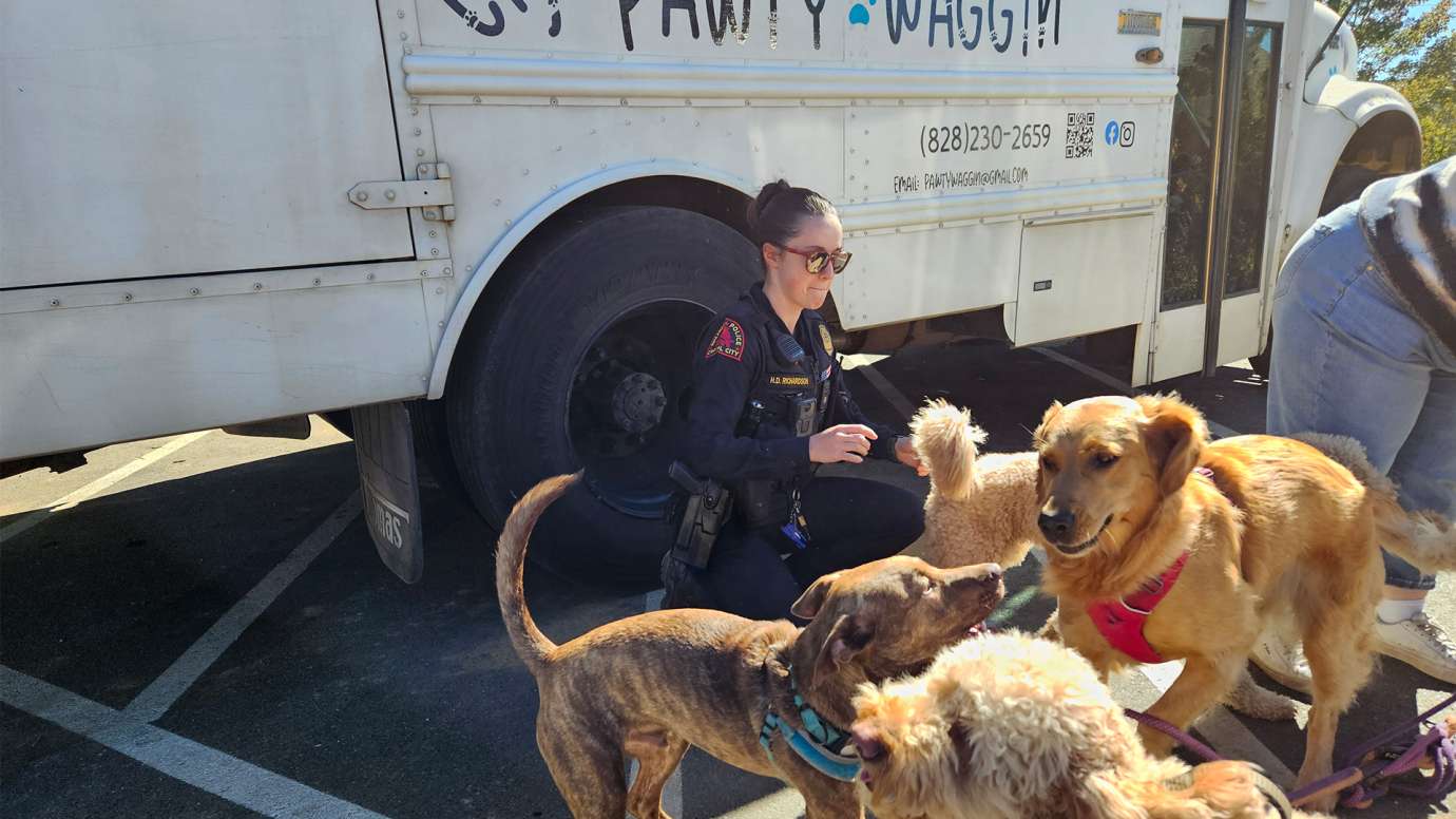 Raleigh police officer pets several dogs in front of "pawty waggin" rescue van