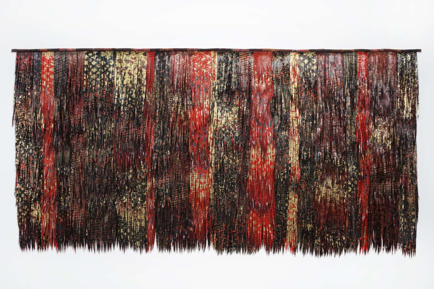 Two dimensional fiber sculpture with feather like fabric in deep reads and browns in a large rectangular shape.