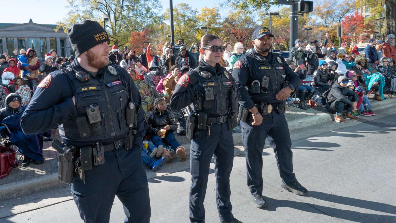 Three officers from RPD enjoy the parade. Parade crowd sits behind them