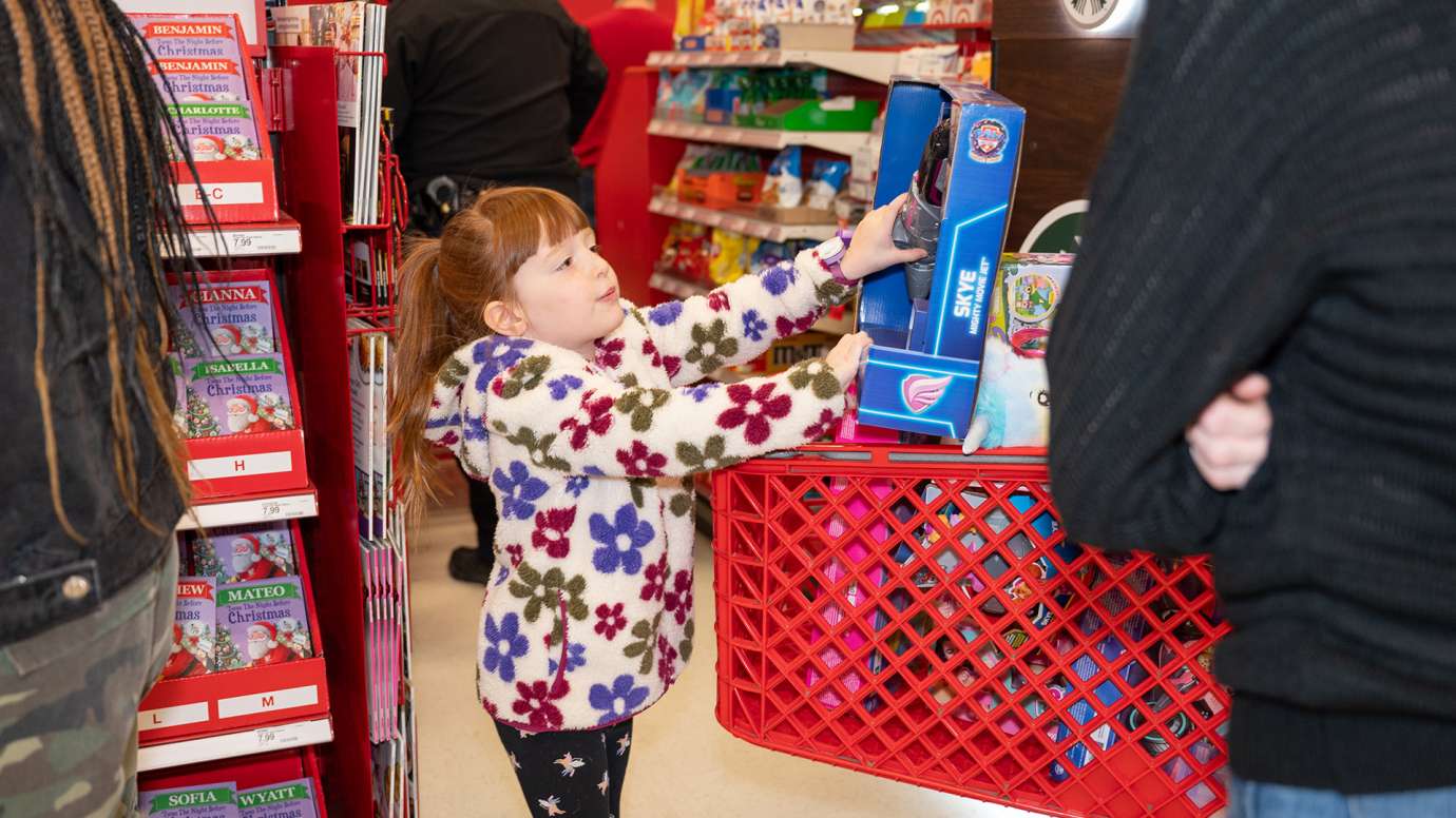 Young girl reaches to put a toy in the shopping cart.