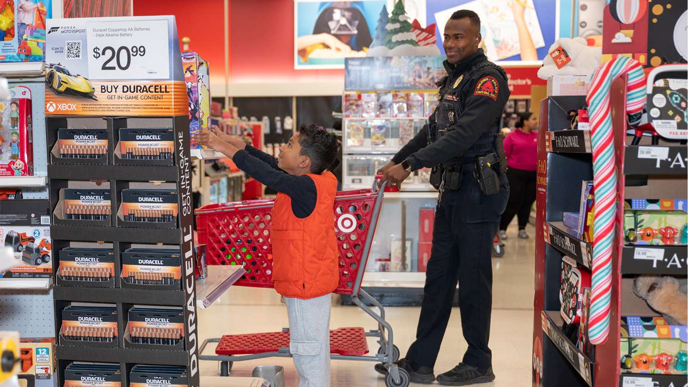 An officer pushes a cart while a young boy reaches up to pull a toy off a shelf.