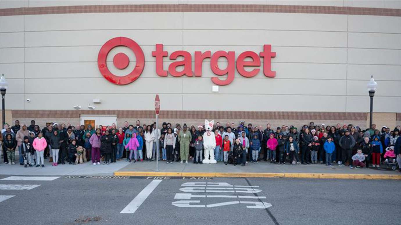 All participants, family members, and officers stand under the large Target sign posing for the camera. The Target mascot stands in the middle.