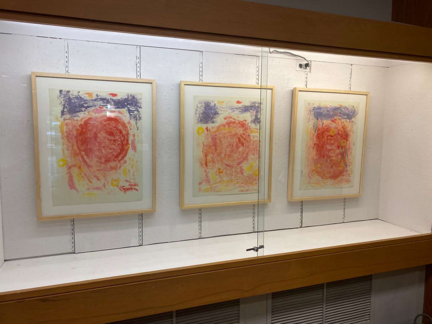 Three Monoprints hanging behind glass 