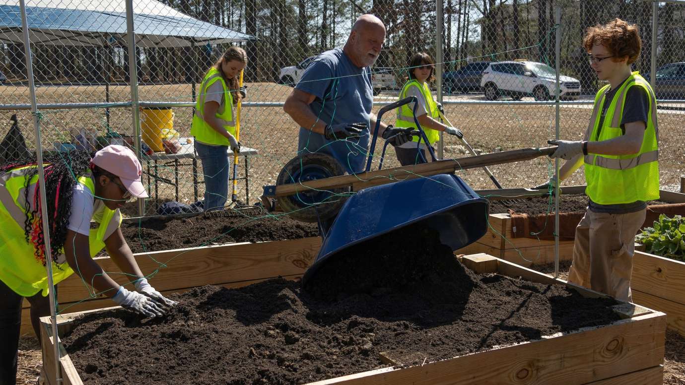 people putting soil in a garden bed