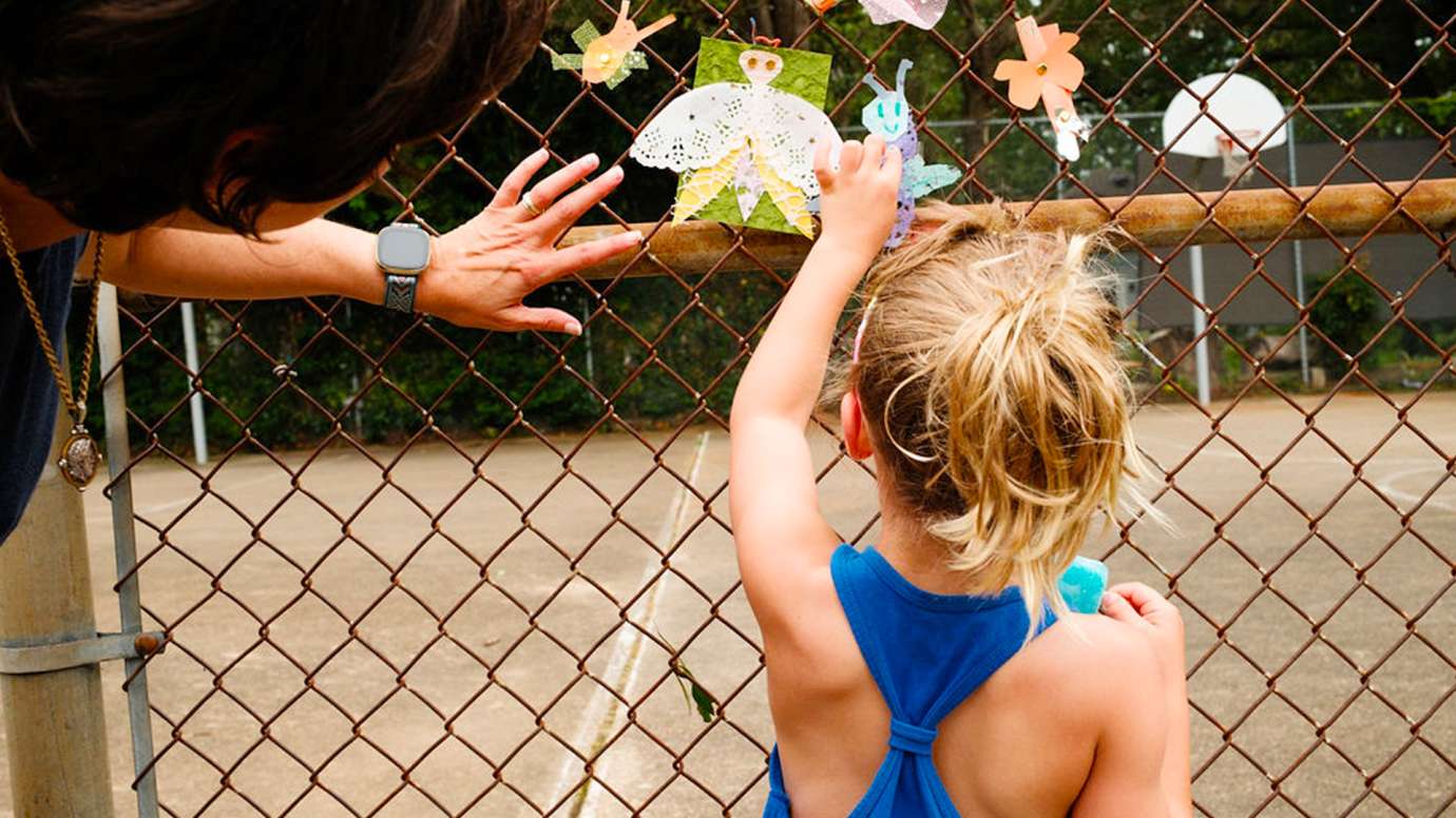 Artist Jean Gray Mohs and a young girl pin up paper insects on a fence