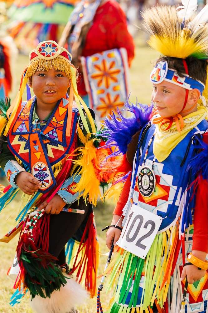 A photo of two children dressed in ceremonial Native American clothing with bright colors.