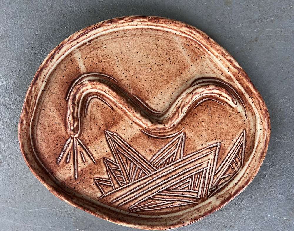 A round, brown pottery dish with a snake etched in the try of the dish