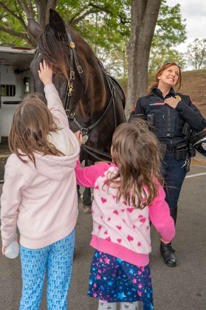 Two children pet Willow's nose with officer standing next to Willow