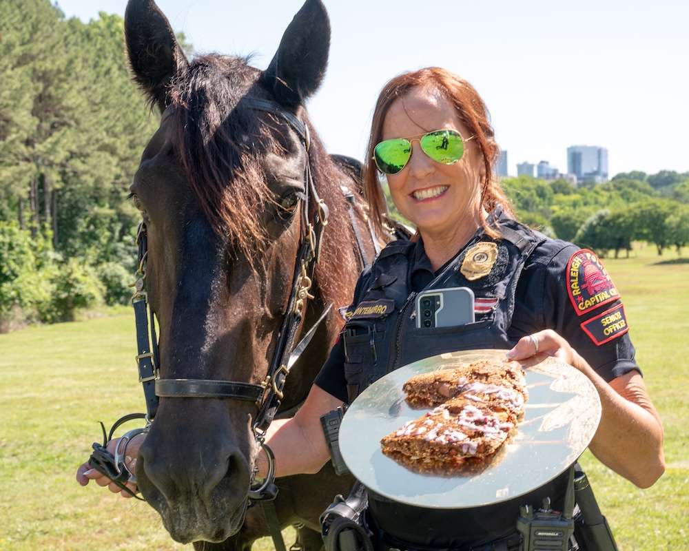 Officer Montemurro holds Willow's rein in one hand and a plate with food shaped in a horse's head