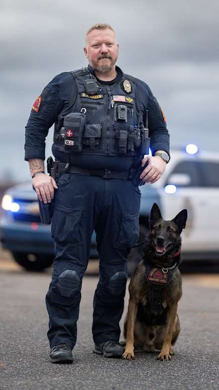Officer Green stands by Hugo on a paved surface with police car in background