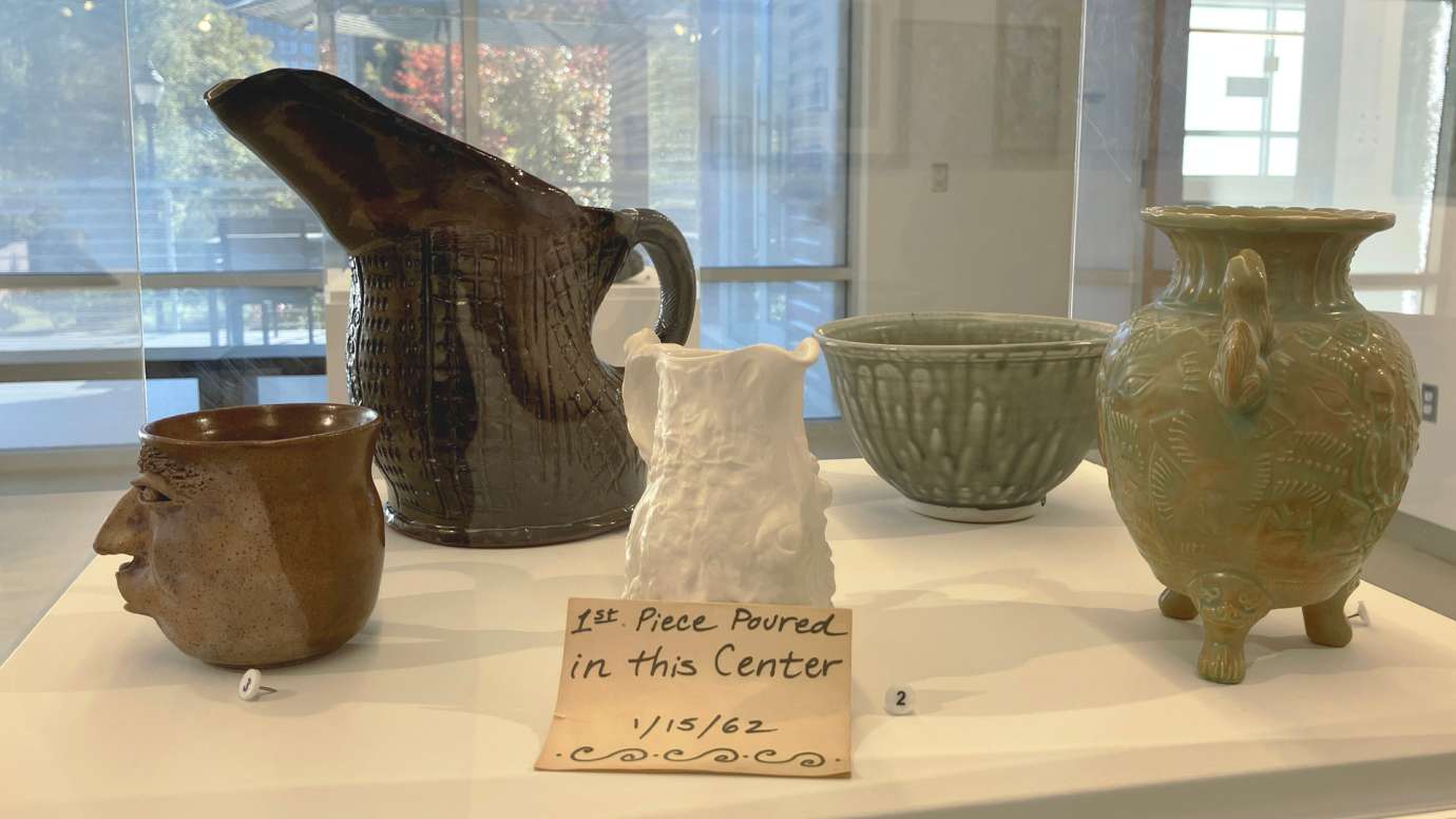  Five pottery pieces in a display case in the gallery, including a white pitcher which was the first piece poured at Pullen Arts Center in 1962