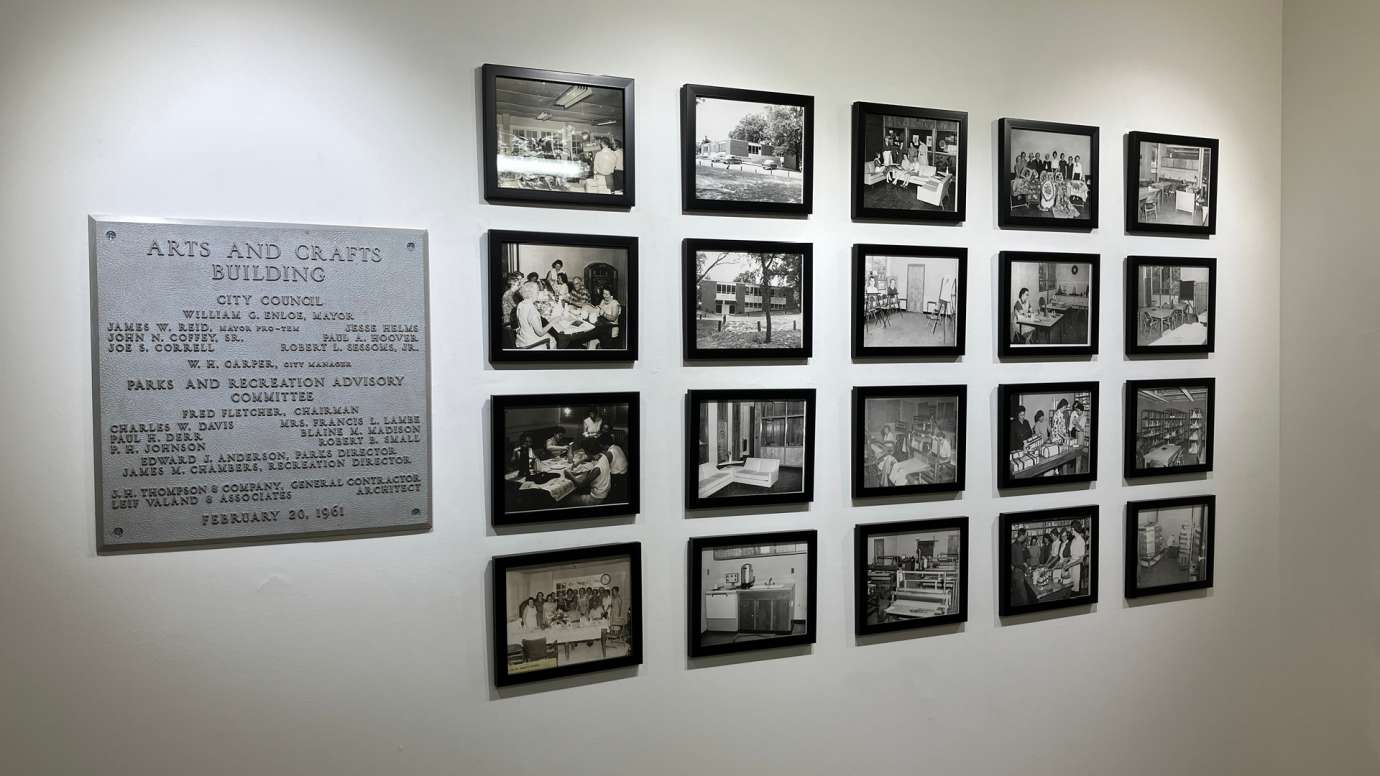 In the gallery, plaque for the original Arts and Crafts building installed alongside a grid of black and white of the original Pullen Arts Center