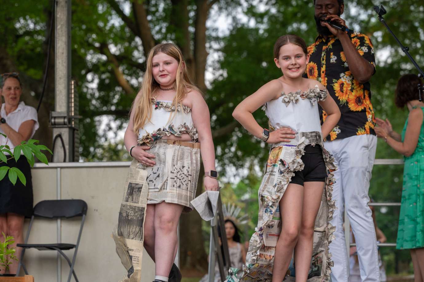 Two girls pose on stage in outfits made of recycled materials.