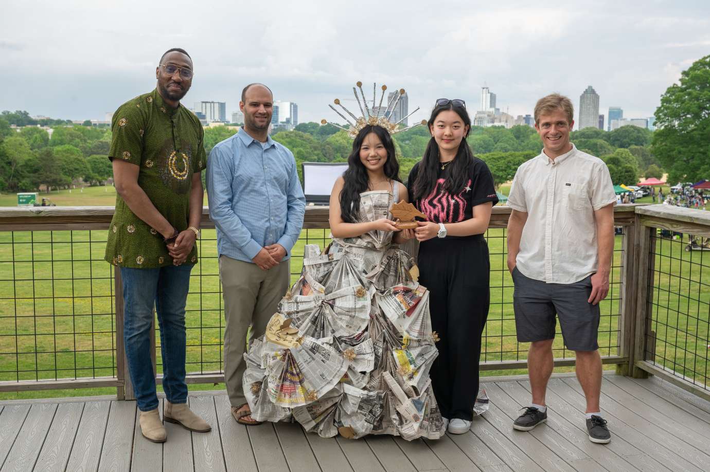 Three men and two women pose in Dix Park. The woman in the center wears the outfit she made of recycled material and holds her first place prize.