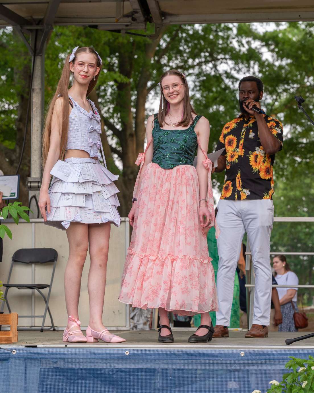 Two women pose on stage in their outfits made of recycled material.