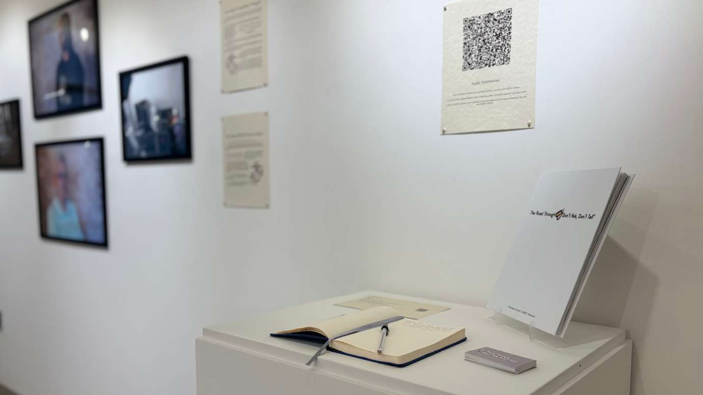 Installation of Don't Ask Don't Tell exhibit featuring a book to sign, qr code, andportrait photos and written statements at Pullen Arts Center