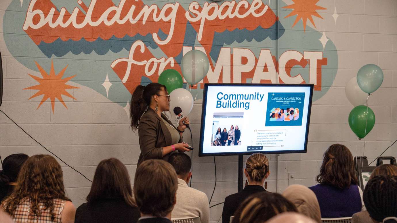 A presenter standing in front of a screen and talking to a group of people