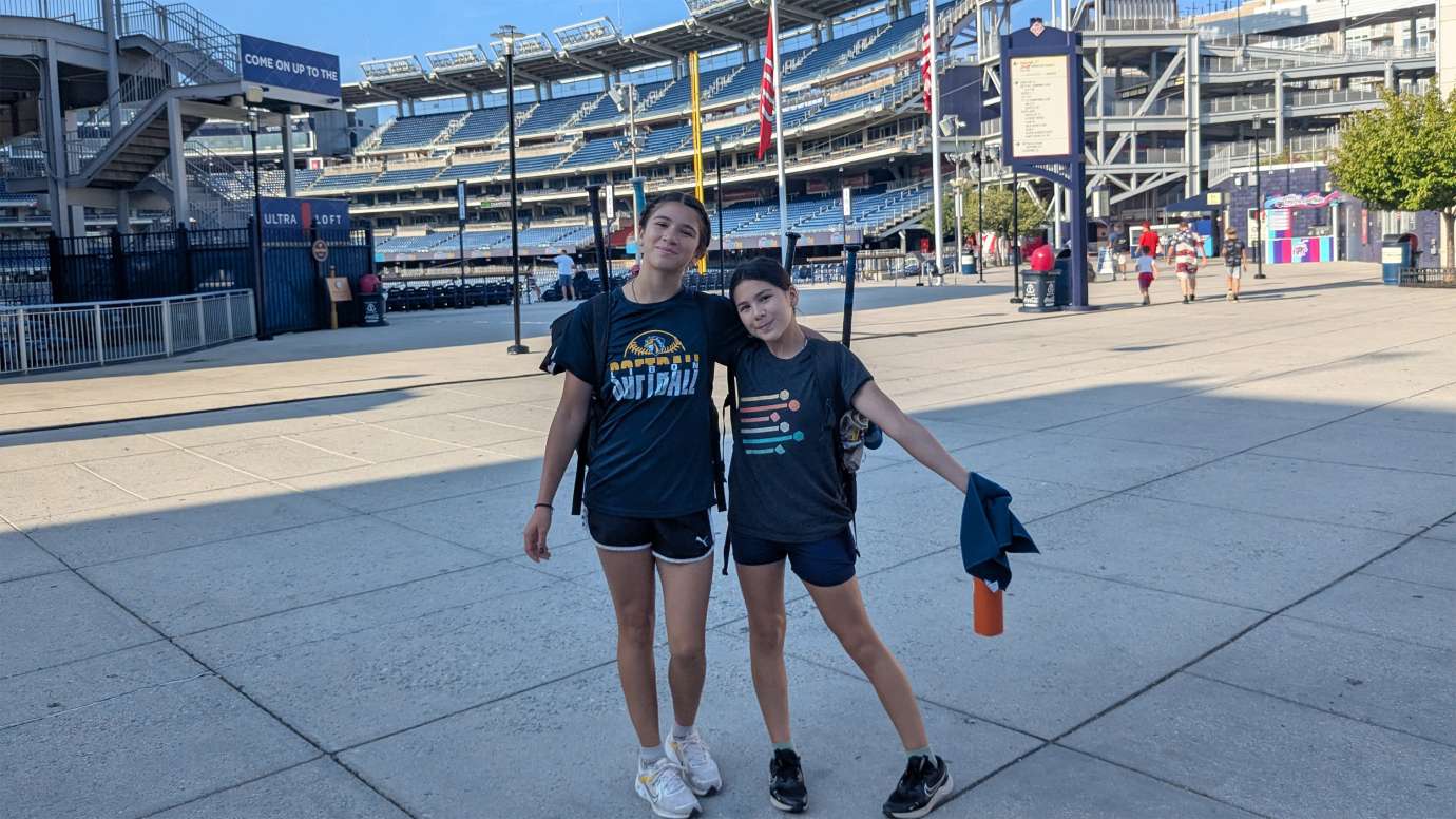 two young people standing outside of a large baseball stadium
