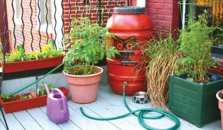 A red rain barrel on a patio with plants and watering can