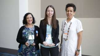 three women smiling, two of them are holding glass awards