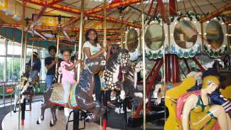 Family with two girls smiling on the carousel horses at chavis park