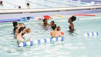 A group of parents and their tots listening to instructor inside the therapy pool at Pullen Park Aquatic Center