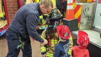 Two boys checking out a firefighter with his mask on and a EMT 
